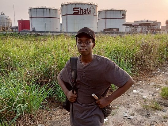 A student standing in tall grass in front of storage tanks